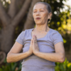 Mulher idosa meditando com a palma das mãos unidas.