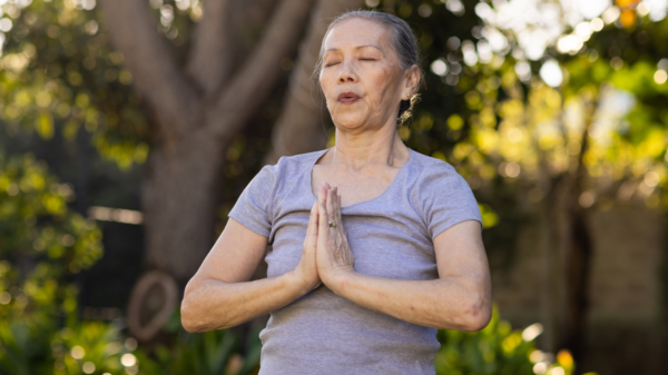 Mulher idosa meditando com a palma das mãos unidas.