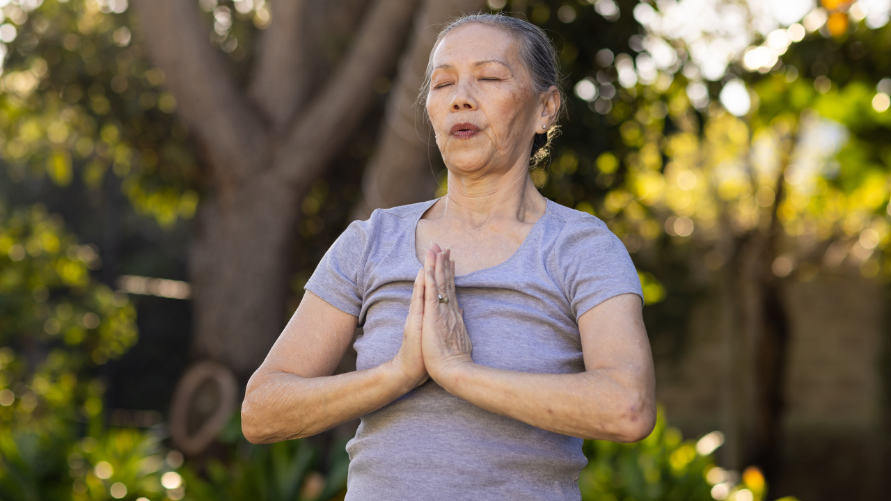 Mulher idosa meditando com a palma das mãos unidas.