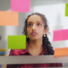 Mulher negra jovem olhando para uma parede cheia de post-it.