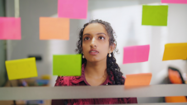 Mulher negra jovem olhando para uma parede cheia de post-it.