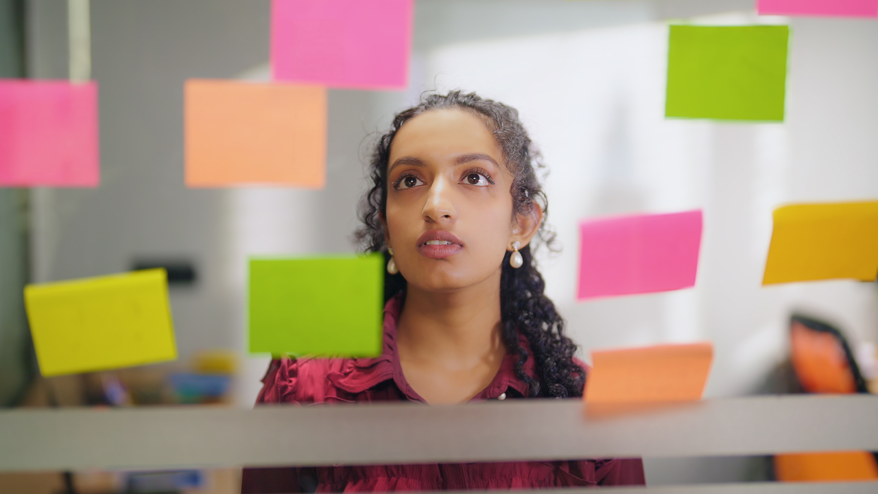 Mulher negra jovem olhando para uma parede cheia de post-it.