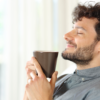 Homem segurando uma xícara de café, com expressão de satisfação, apreciando a bebida.