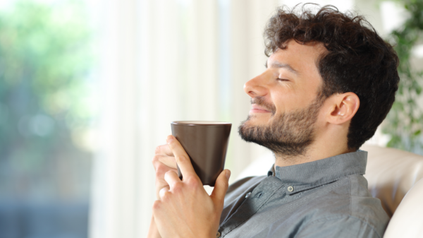 Homem segurando uma xícara de café, com expressão de satisfação, apreciando a bebida.