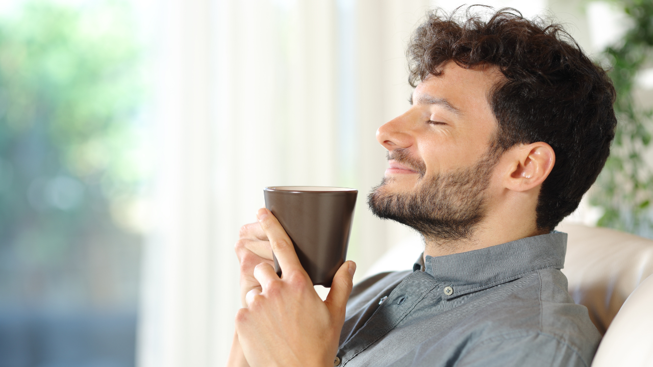 Homem segurando uma xícara de café, com expressão de satisfação, apreciando a bebida.