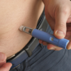 Pessoa aplicando uma caneta injetora de medicamento na região abdominal