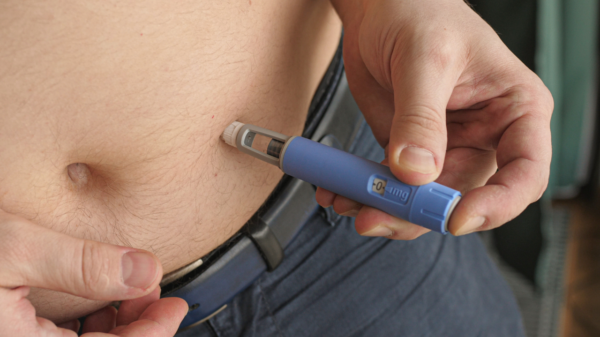 Pessoa aplicando uma caneta injetora de medicamento na região abdominal