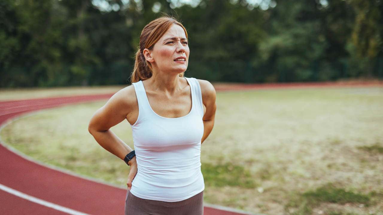 Mulher sentindo desconforto nas costas durante a corrida em uma pista de atletismo ao ar livre.
