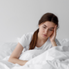 Mulher sentada na cama, coberta, com expressão de preocupação e dificuldade para dormir devido à ansiedade noturna.