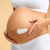 Gestante aplica creme hidratante na barriga durante a gravidez, reforçando os cuidados com a pele no período gestacional.