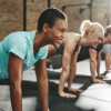 Grupo de pessoas praticando exercício físico em academia, realizando prancha no chão durante treino coletivo