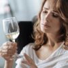 Mulher branca loira olhando preocupada para uma taça de champagne.