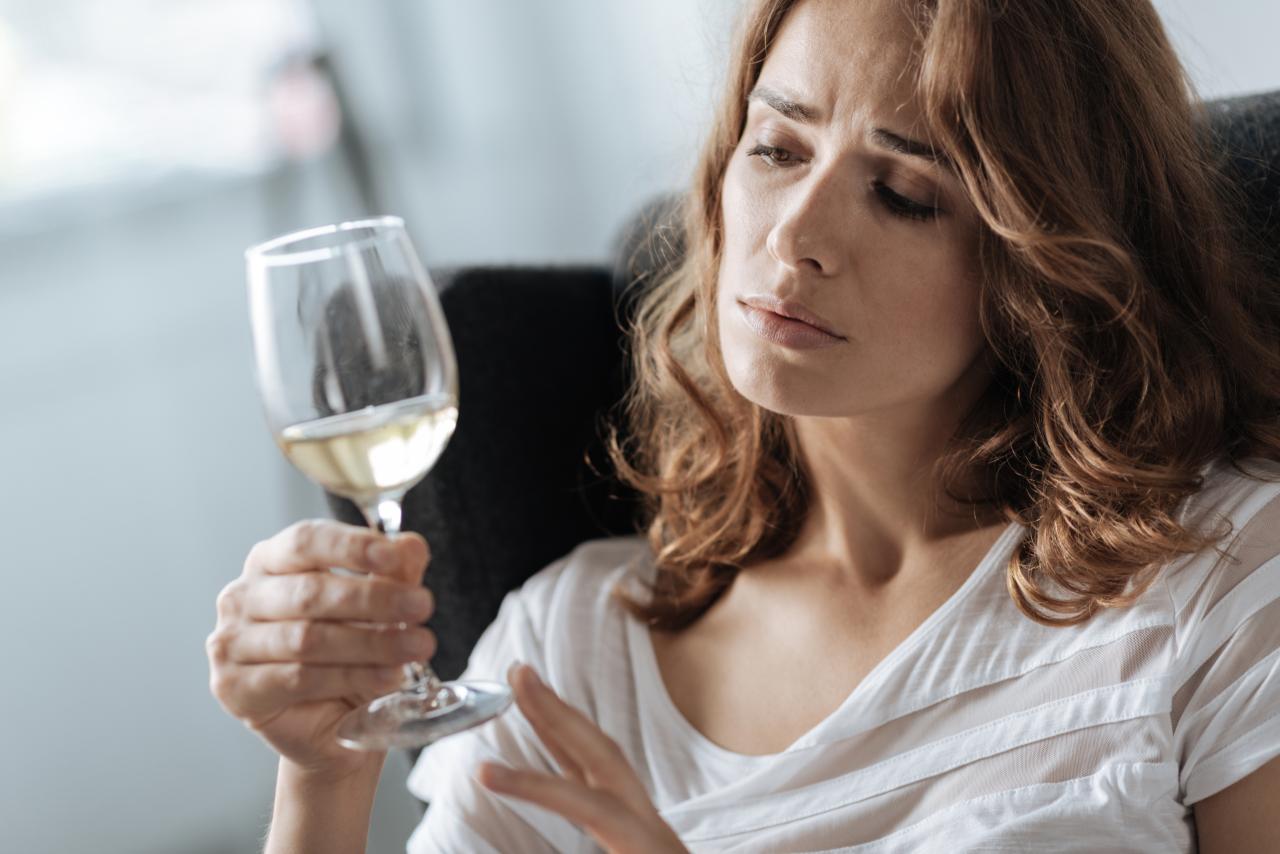 Mulher branca loira olhando preocupada para uma taça de champagne.