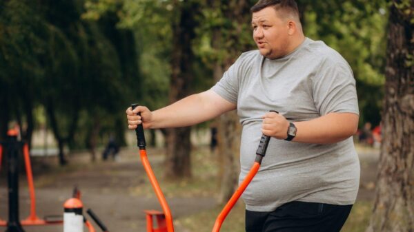 Homem branco, gordo, usando camiseta cinza, fazendo exercício em um parque.
