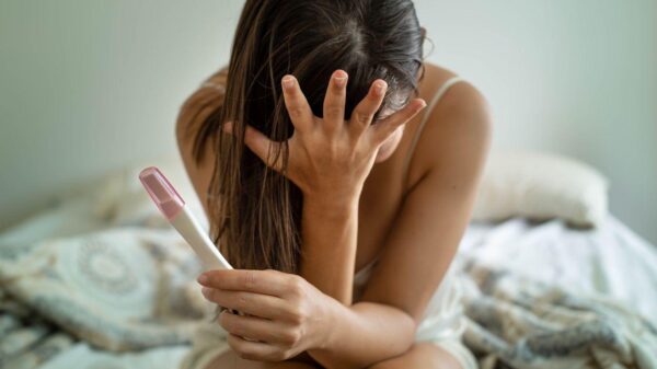 Mulher com a mão no rosto e segurando um teste de gravidez com semblante preocupado.