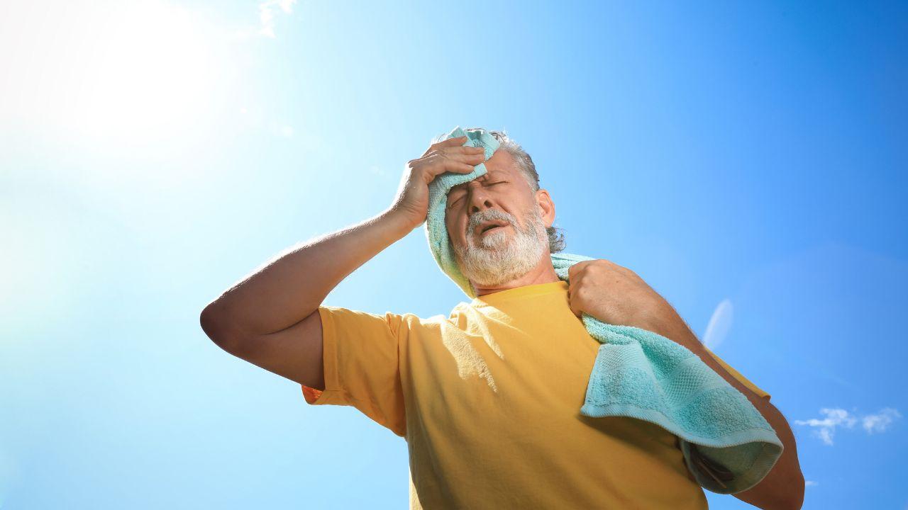 Imagem de um idoso, passando uma toalha no rosto em um dia de muito calor
