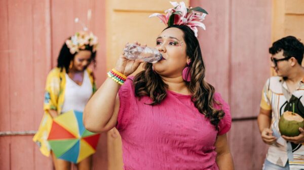Imagem de uma mulher, de blusa rosa e tiara com lírios rosa, bebendo água no bloquinho