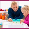 Professora sorridente acompanha menina pequena em atividade escolar colorida, estimulando aprendizado e criatividade em ambiente educativo.