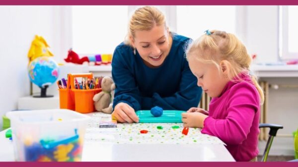 Professora sorridente acompanha menina pequena em atividade escolar colorida, estimulando aprendizado e criatividade em ambiente educativo.