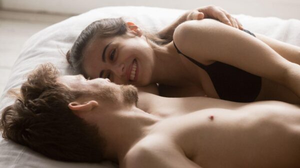 Imagem de um casal, na cama, de roupas íntimas, sorrindo um para o outro
