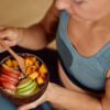 Foto mostra um pote com frutas cortadas: maça, pera e ameixa. Uma mulher segura o pote.