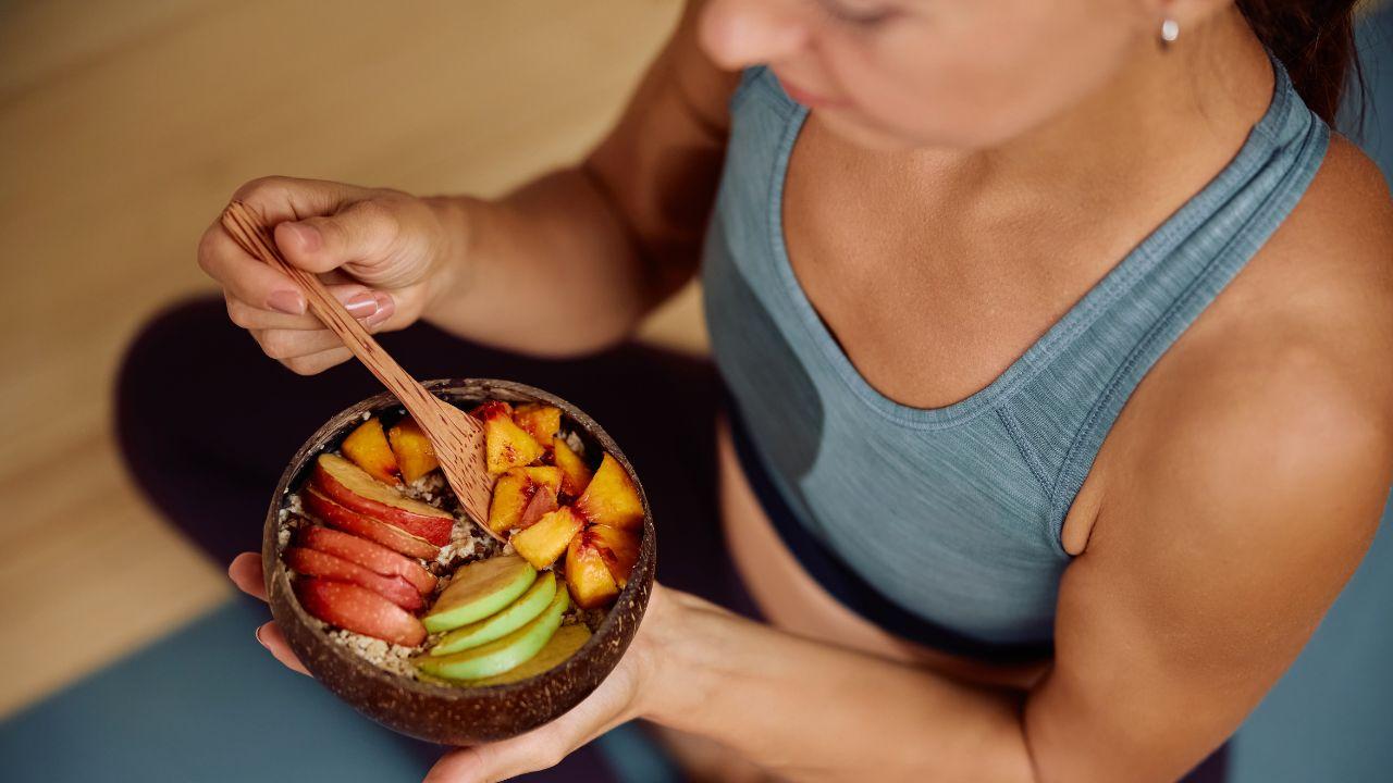 Foto mostra um pote com frutas cortadas: maça, pera e ameixa. Uma mulher segura o pote.