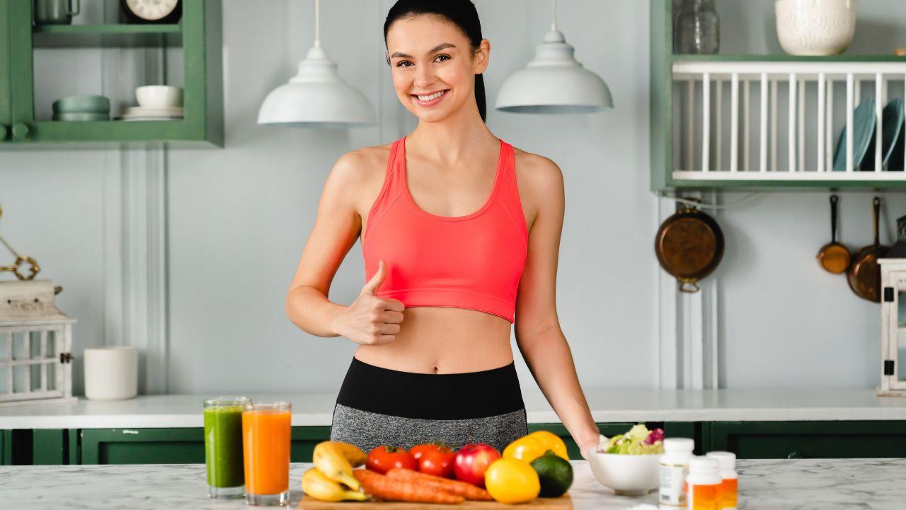 Mulher branca com top na frente de uma mesa com frutas e copos de suco.