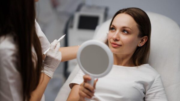 Foto mostra uma mulher sentada numa mesa médica com um espelho ao lado de uma médica.