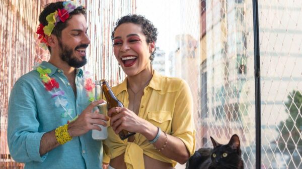 Mulher e homem com roupas coloridas brindando uma cerveja.