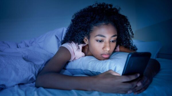Mulher negra mexendo no celular deitada na cama a noite.