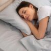 Foto mostra uma mulher branca deitada na cama dormindo.