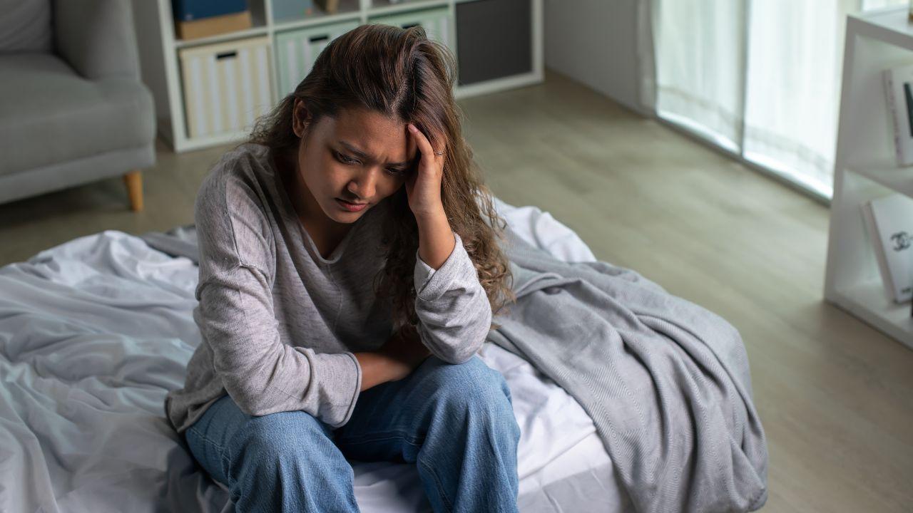 Imagem de uma pessoa ansiosa, sentada na cama, com as mãos na cabeça