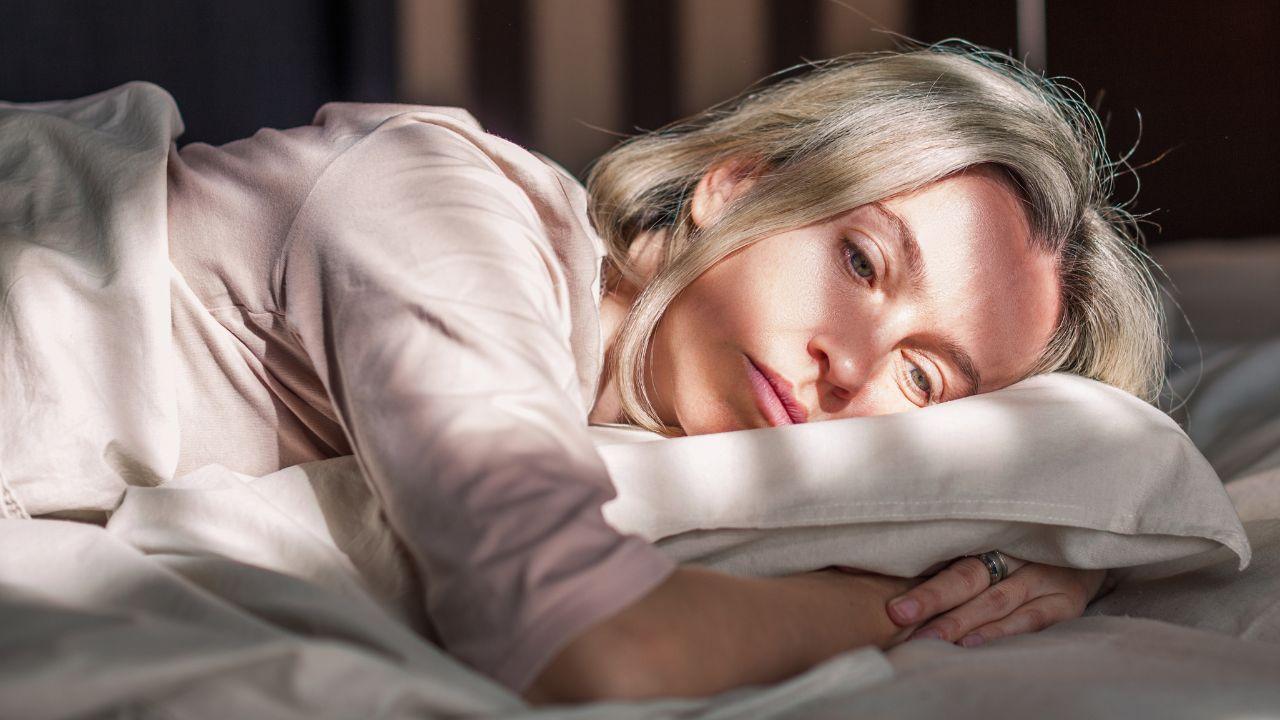 Imagem de uma mulher de meia idade deitada na cama com semblante triste
