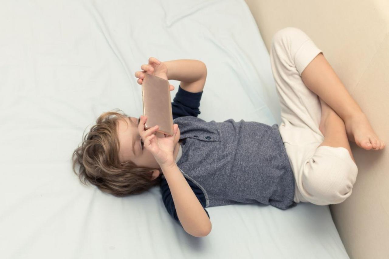 Criança usando dispositivo móvel em casa ilustra discussão sobre uso de telas na infância após novo guia da Academia Americana de Pediatria.