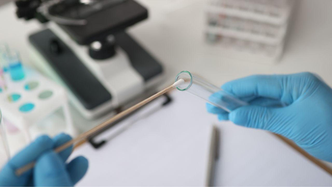 Imagem de mãos passando um cotonete em um canudo de laboratório para fazer um exame
