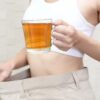 Imagem de uma mulher segurando uma xícara de chá e mostrando a calça larga na barriga