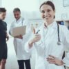 Imagem de uma médica fazendo joia com o dedão e um médico conversando com um atleta no fundo