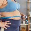 Imagem de uma mulher obesa, com roupa de academia, medindo a circunferência de sua cintura
