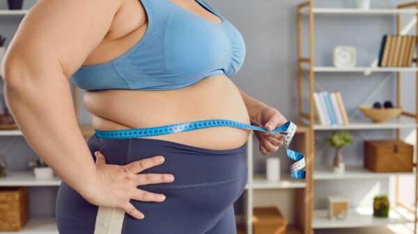 Imagem de uma mulher obesa, com roupa de academia, medindo a circunferência de sua cintura