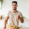 Homem na cozinha, na frente da mesa com comidas saudáveis. Ele faz o sinal de joinha.