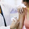 Mulher sentada enquanto toma vacina de uma médica.