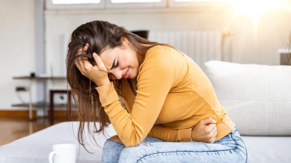 Mulher sentada no sofá com a mão na barriga apresentando desconforto abdominal.