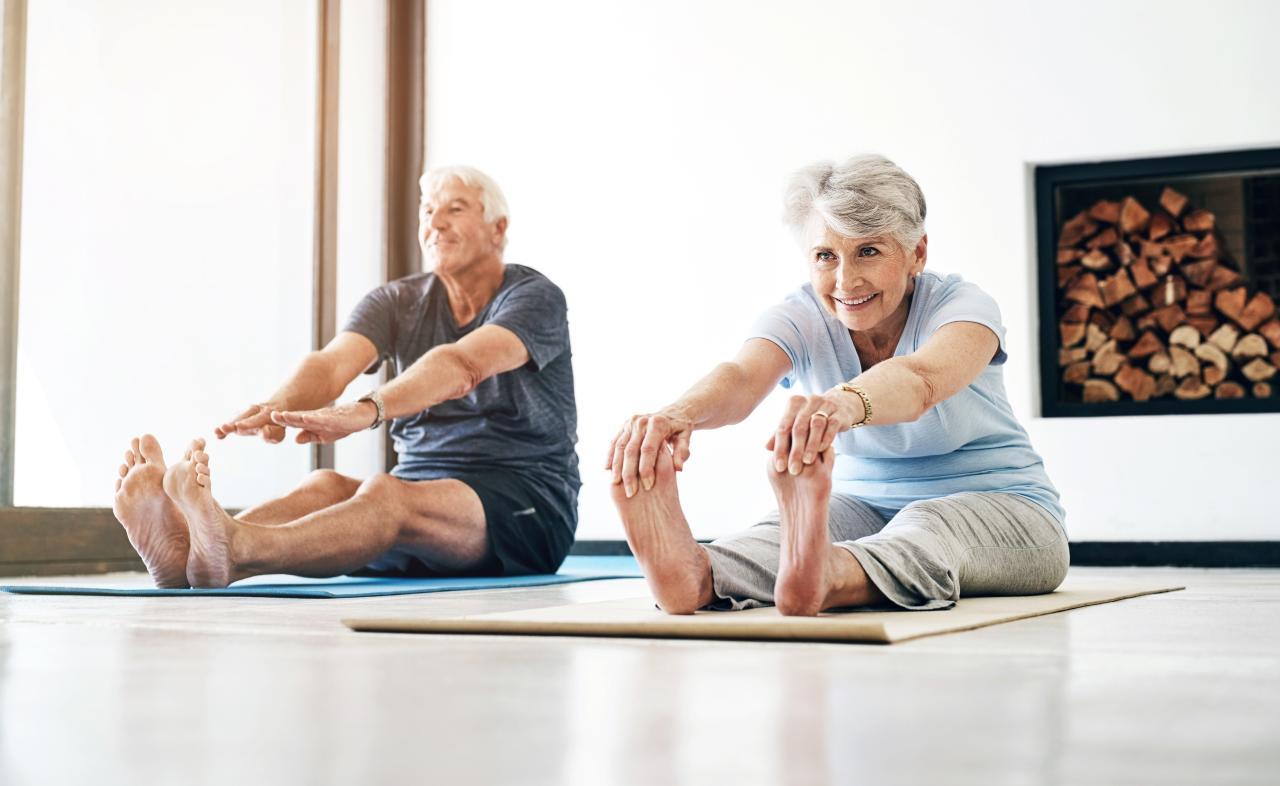 Homem e mulher idosos sentados no chão alongando o corpo.