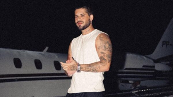 Zé Felipe. Homem branco, cabelo curto castanho, usando camiseta branca na frente de um avião.