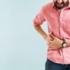 Foto mostra homem com camisa rosa com as mãos na lateral da barriga.