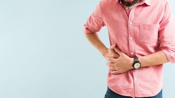 Foto mostra homem com camisa rosa com as mãos na lateral da barriga.
