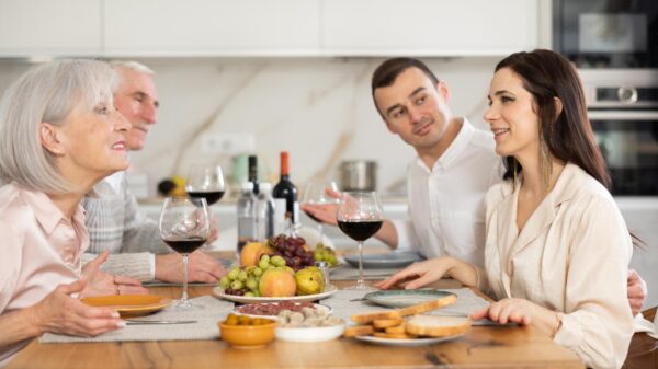 Um casal jovem sentados numa mesa enquanto comem em frente a um casal de idosos que são pais de algum deles.