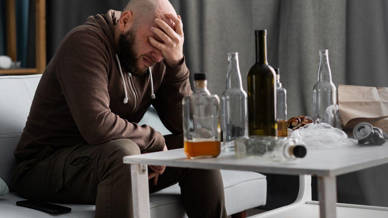 Imagem de um homem apoiado em uma mesa com várias garrafas de bebida