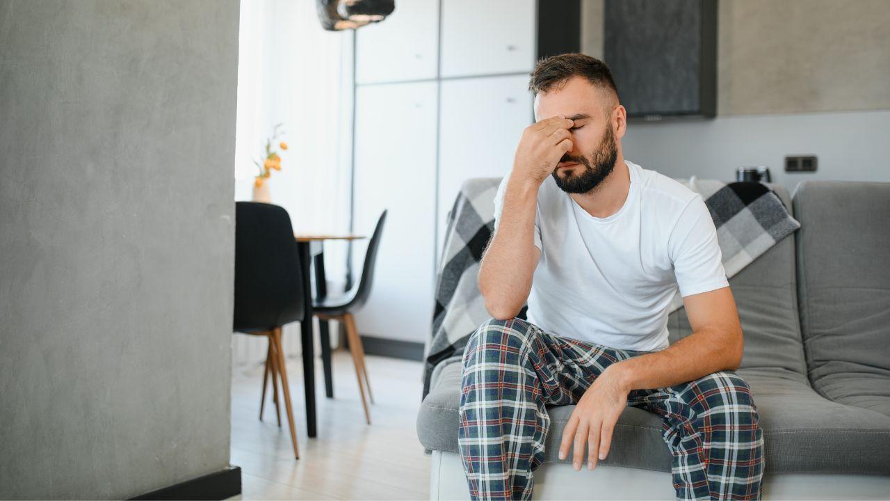 Imagem de um homem sentado de pijama com a mão no rosto