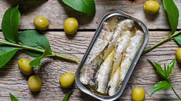 Imagem de uma lata de sardinha aberta com azeitonas em volta na mesa